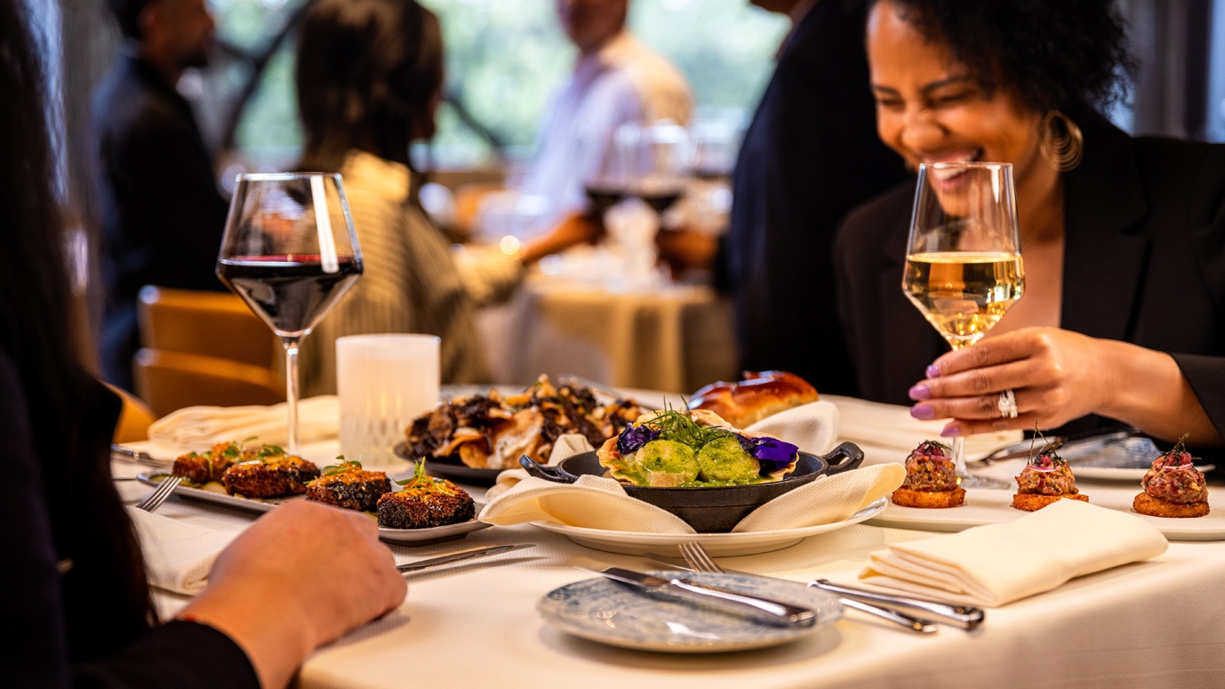 People laughing at a table of food and wine